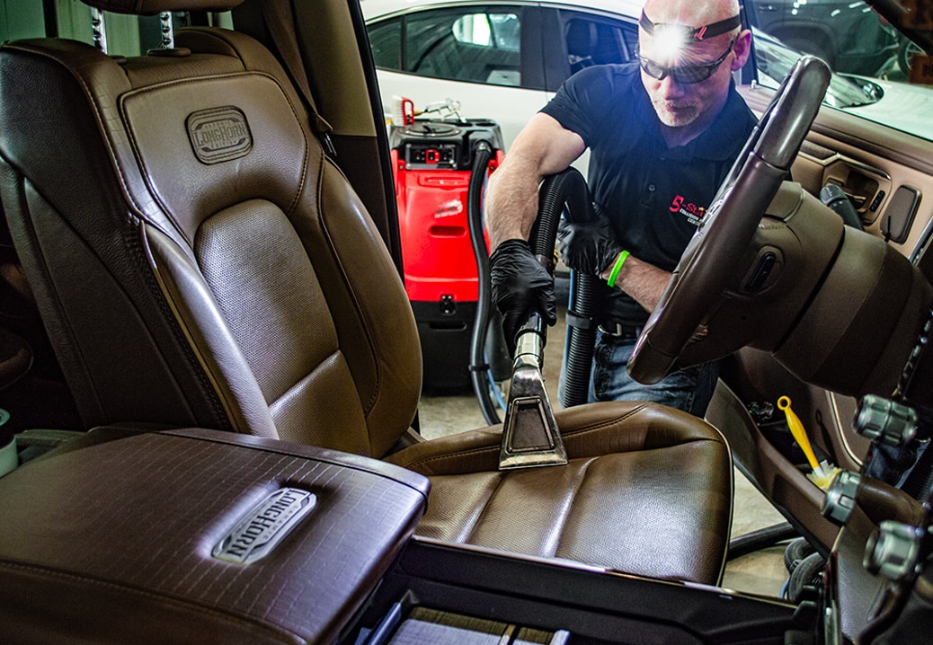 Technician vacuuming out the driver's seat of vehicle.